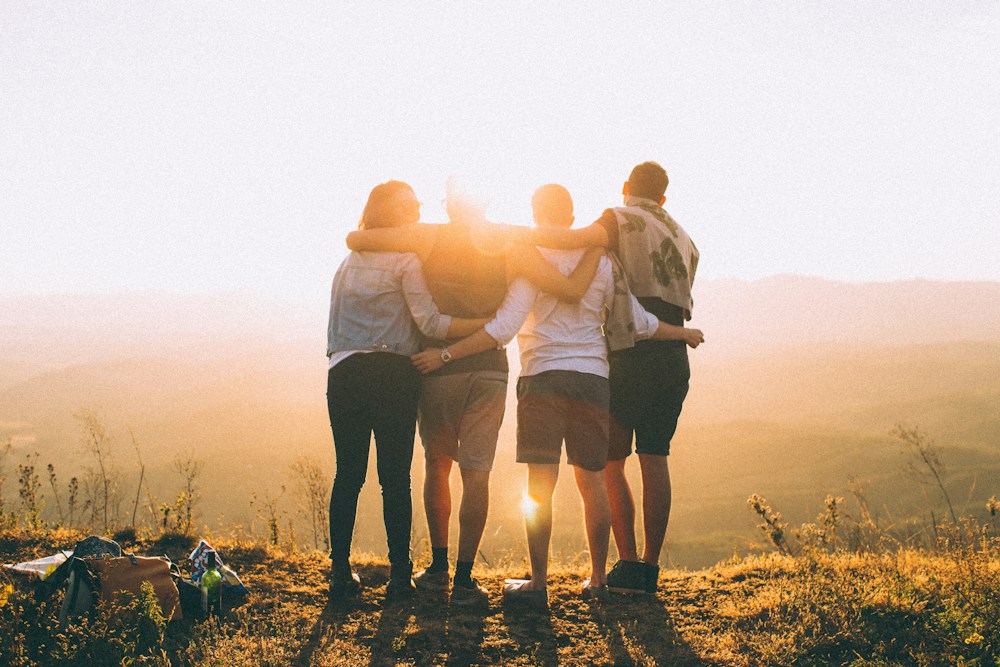 Grupo de amigos abraçados apreciando o pôr do sol ao ar livre
